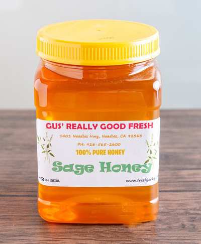 A clear plastic jar with a yellow lid labeled 'Gus' Really Good Fresh 100% Pure Honey Sage Honey'.