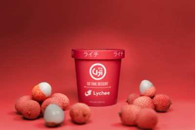 The image shows a red pint container of Uji Time Dessert Lychee Ice Cream with lychee fruits around it.